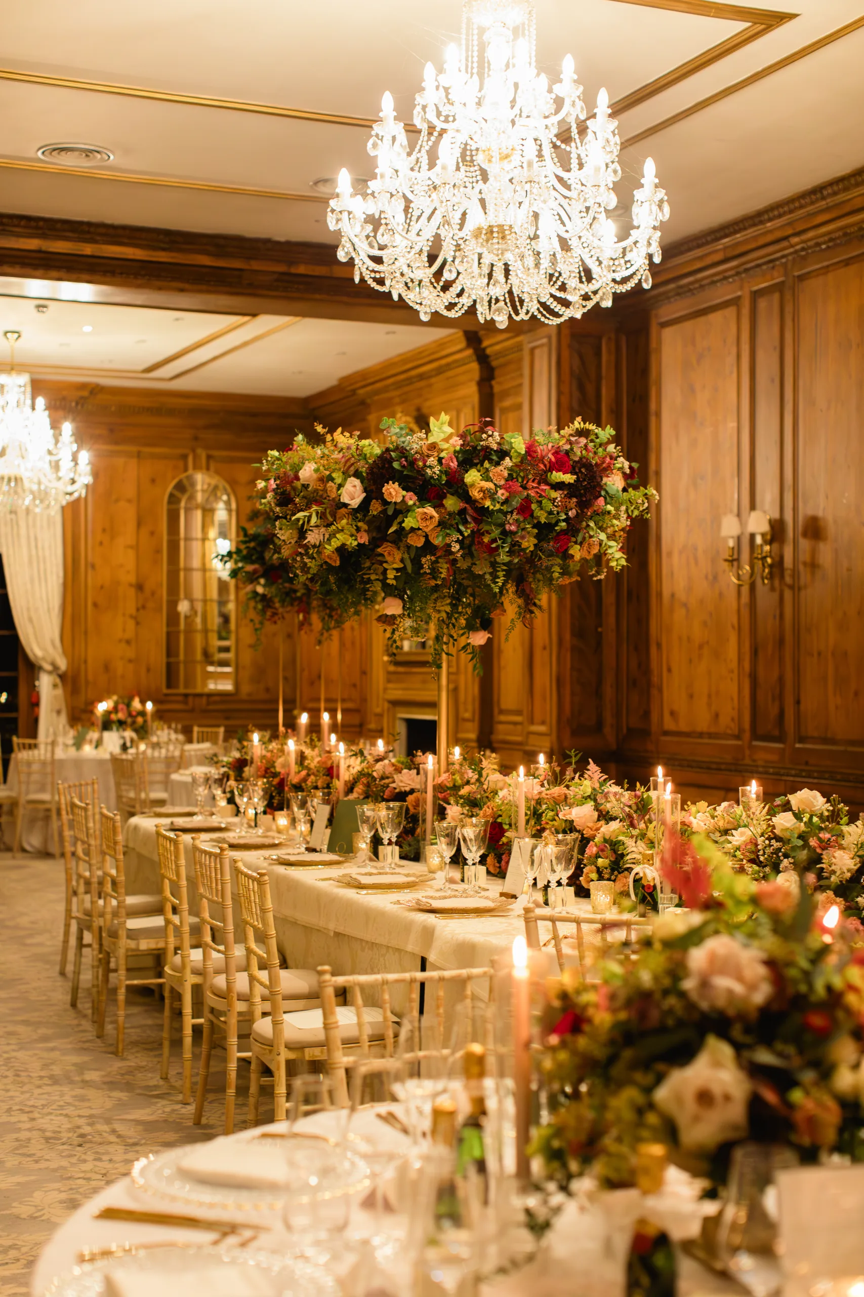 Wood panel room in Hedsor House set up for a wedding, with a mix of round tables and long tables, decorated with multicoloured floral centrepieces.