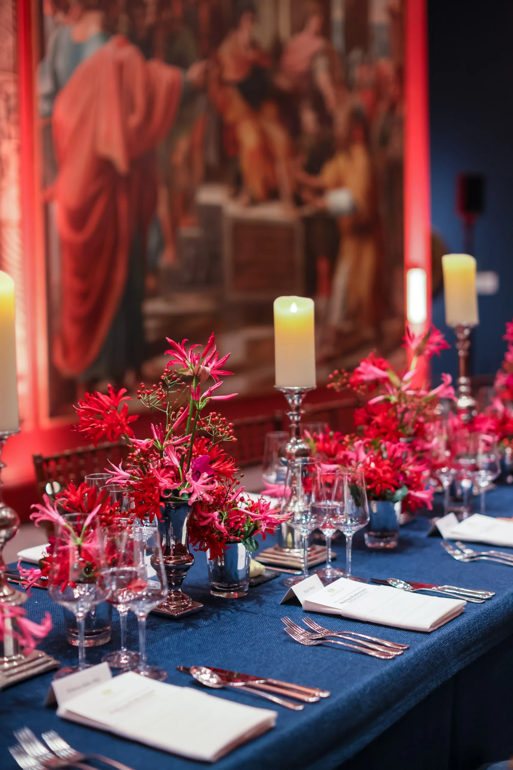 View of a red and blue tablescape set for dinner with small vases of red plant displays