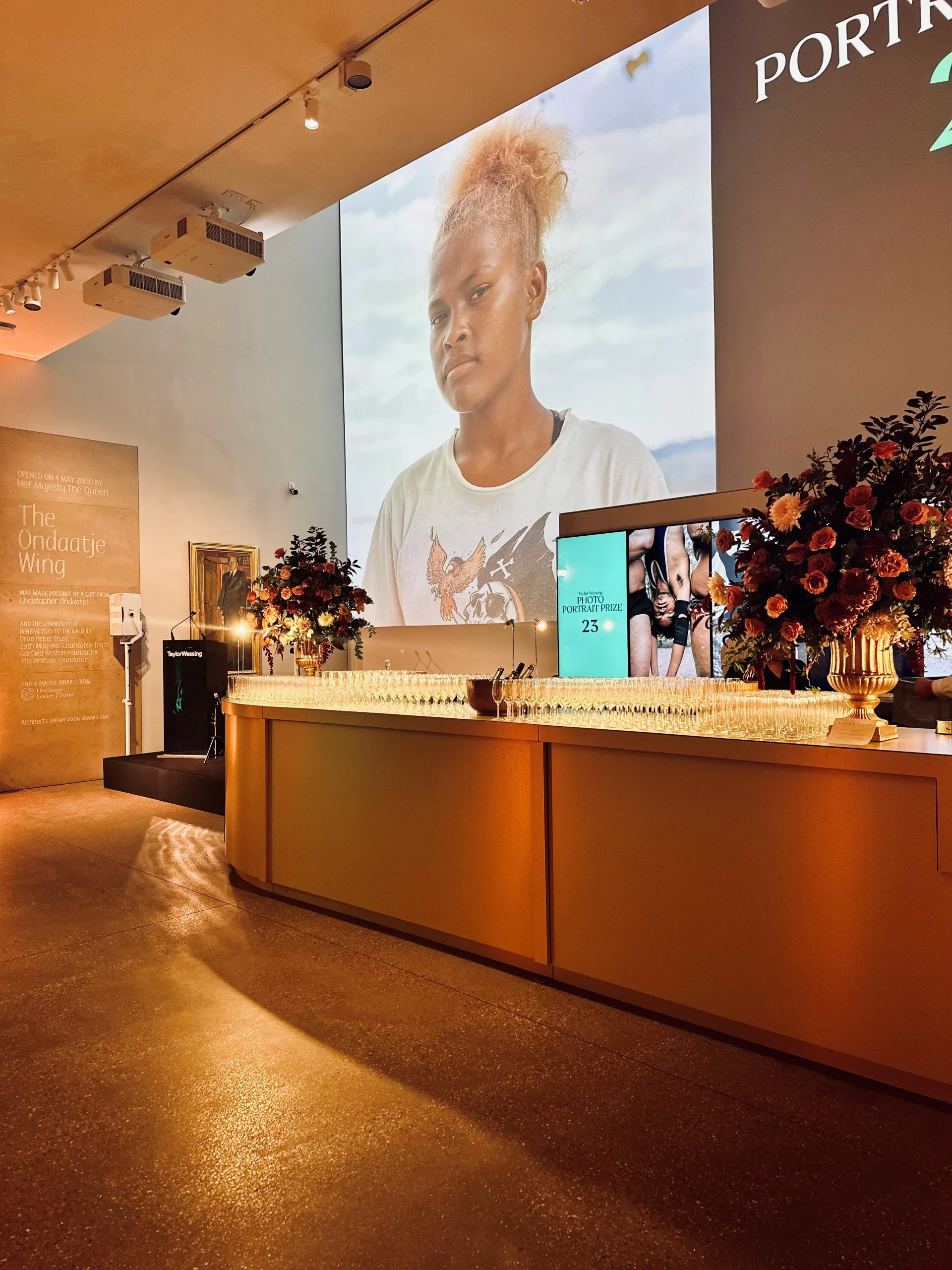 Table of wine glasses and large floral displays under warm golden light in National Portrait Gallery