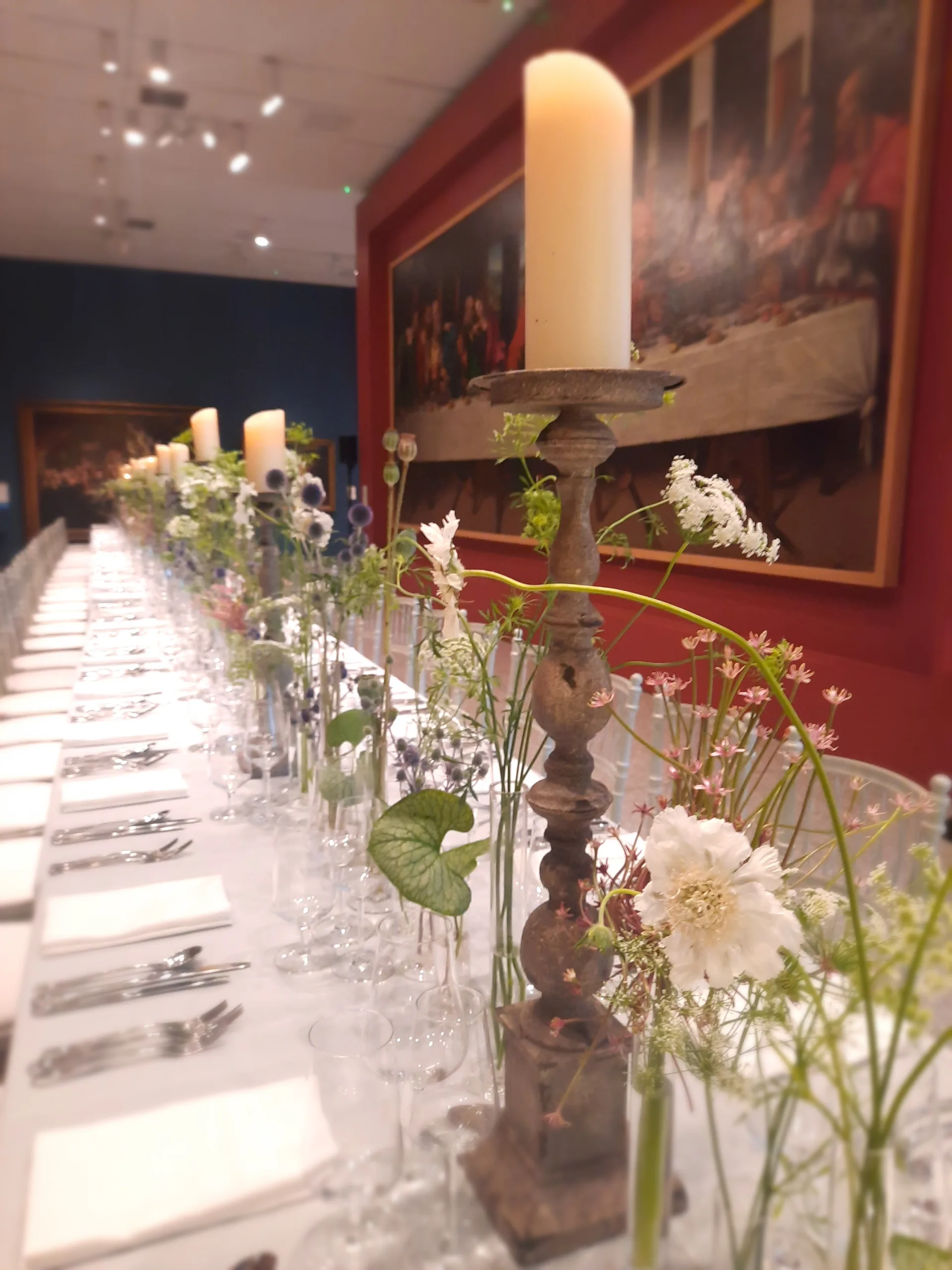 Close-up of white candle with a tall carved candlestick on a white table set for dinner