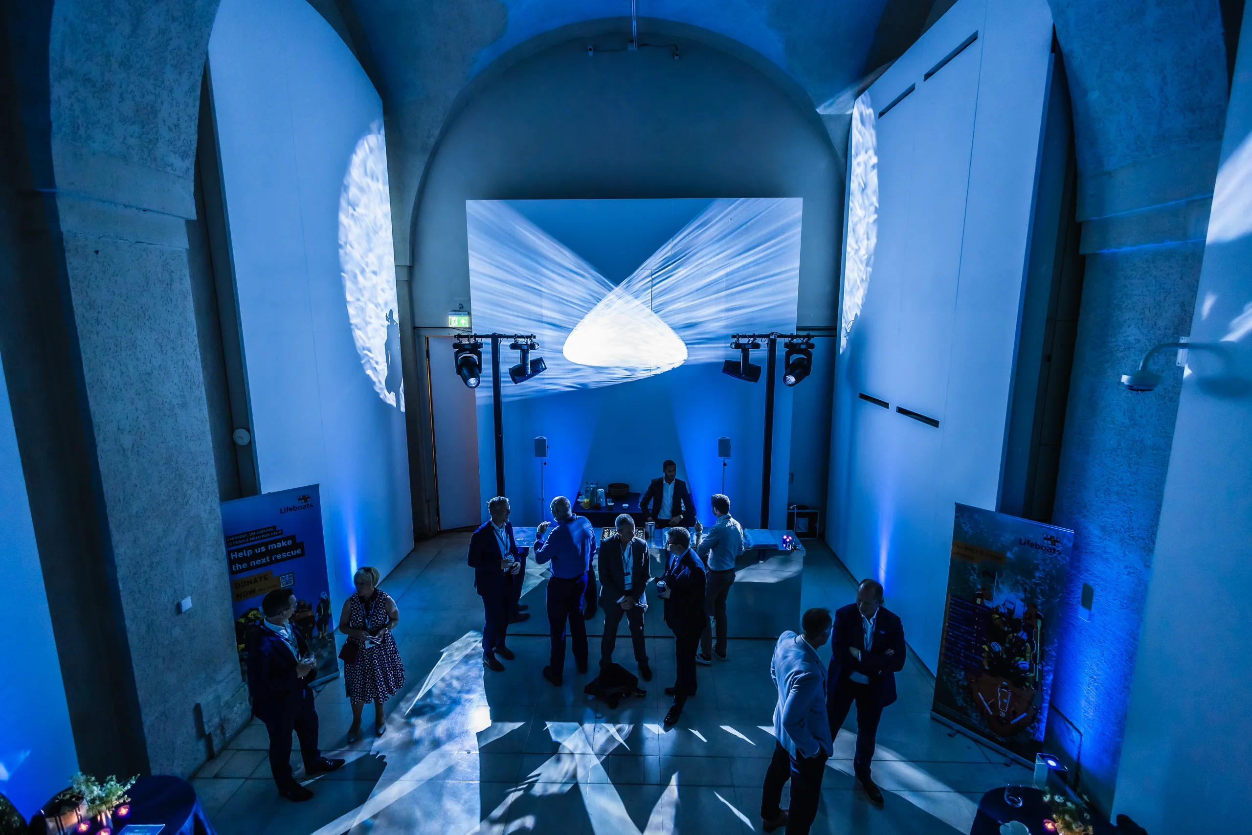 Various people standing around talking under a blue hued room in Somerset House