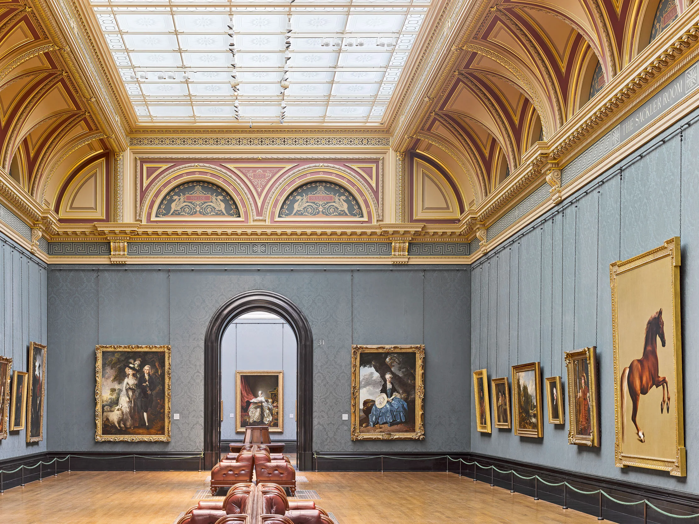 National Gallery room with powder blue walls with hung paintings, brown leather seating in the centre of the room and a large ceiling light.