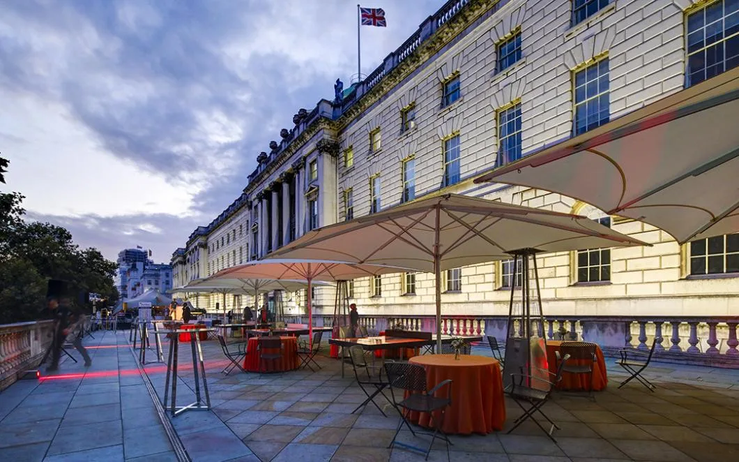 Terrace at Somerset House laid out with chairs and tables with red tablecloths, large cream umbrellas and red lights.