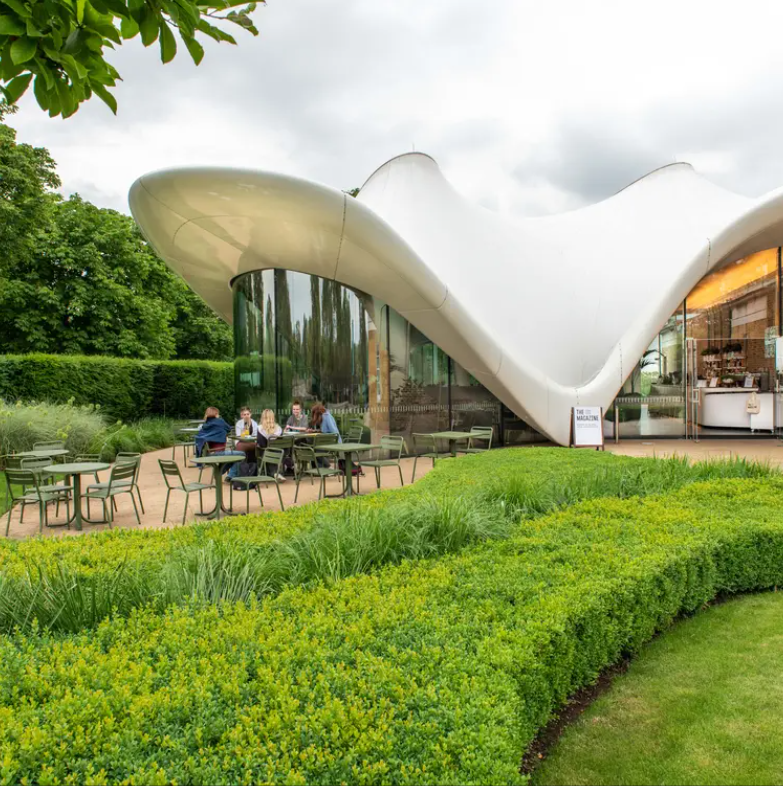 Exterior of Serpentine Gallery cafe with green hedges, patio with olive green tables and chairs