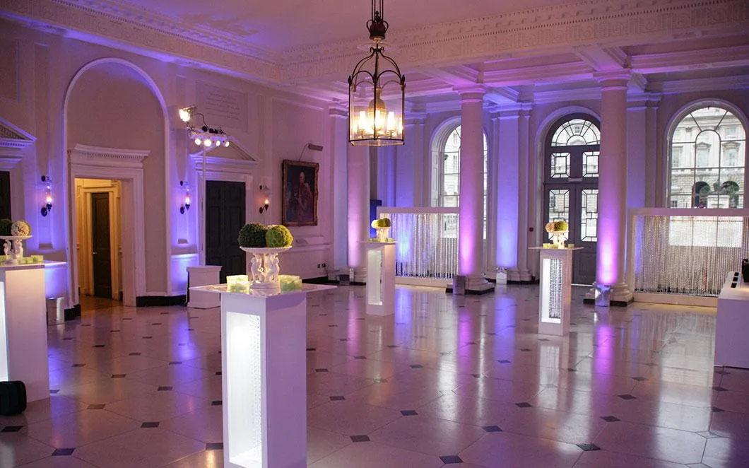 Seamen's Hall in Somerset House set up with pink and purple uplighters at the edges of the room, white lit square podiums with ornaments