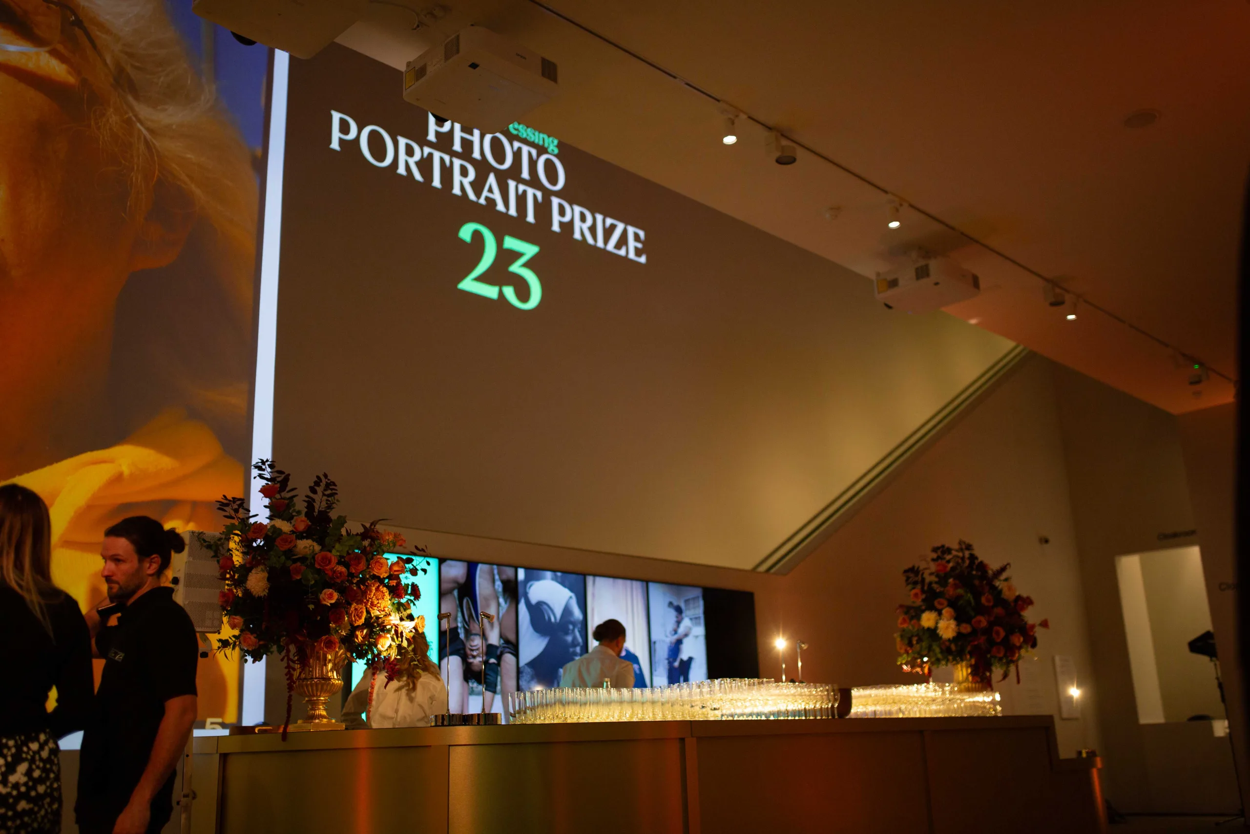 Photo Portrait Prize '23 projection of wall at National Portrait Gallery near table of glasses
