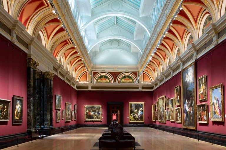 Large gallery room with wine red walls, a selection of portraits, terracotta orange upper mouldings and ice blue roof arches