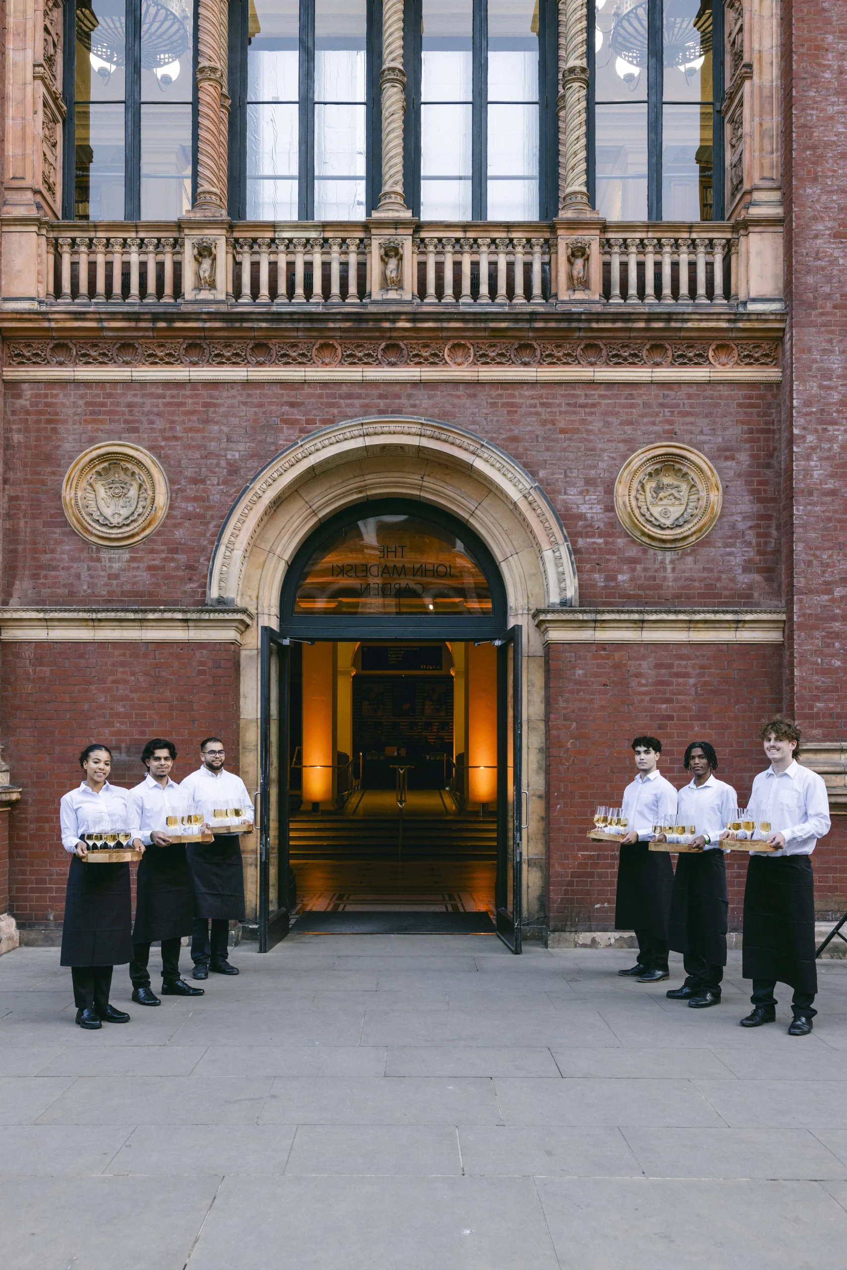 Outside side doorway at The V&A with three wait staff holding trays of drinks on each side.