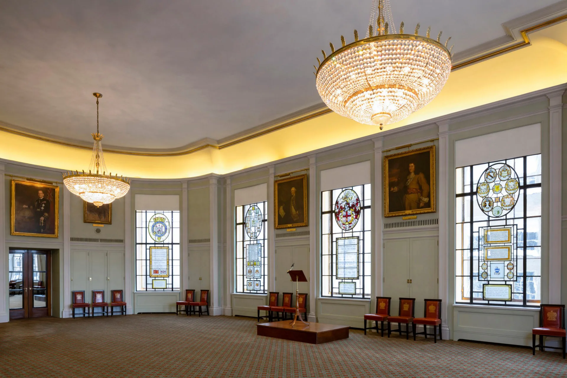 Open room in Trinity House, with yellow lit upper border area, large handing lights and decorative windows around the edge.