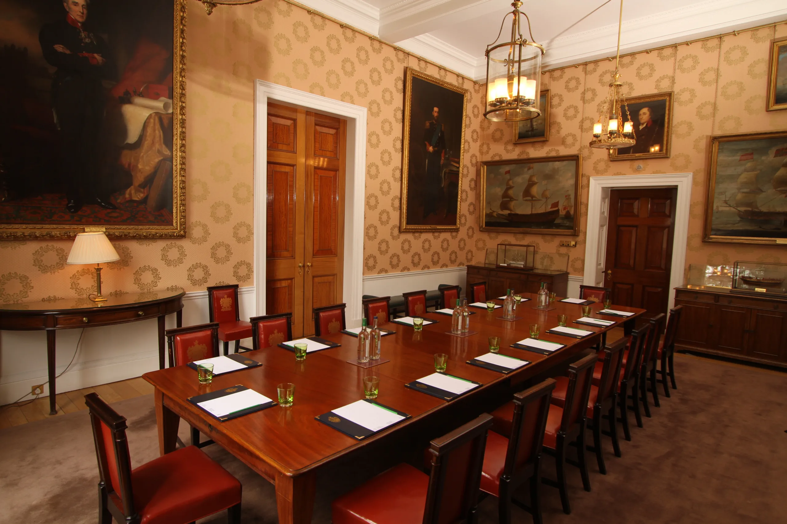 Interior of Trinity House room with large red-wood table with red chairs, set up for a meeting with pads of paper and water glasses.