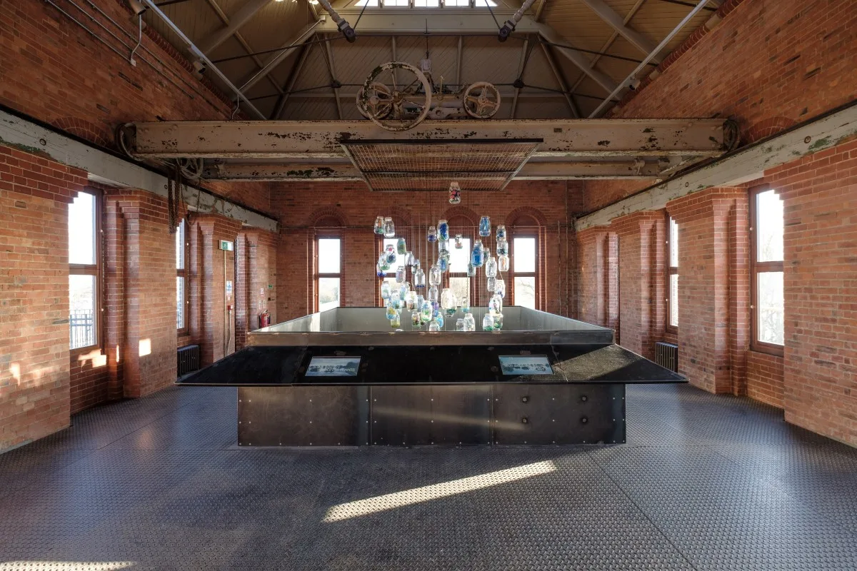 High room in Engine House with central diplay and hanging display, windows around three red brick walls with ceiling light above